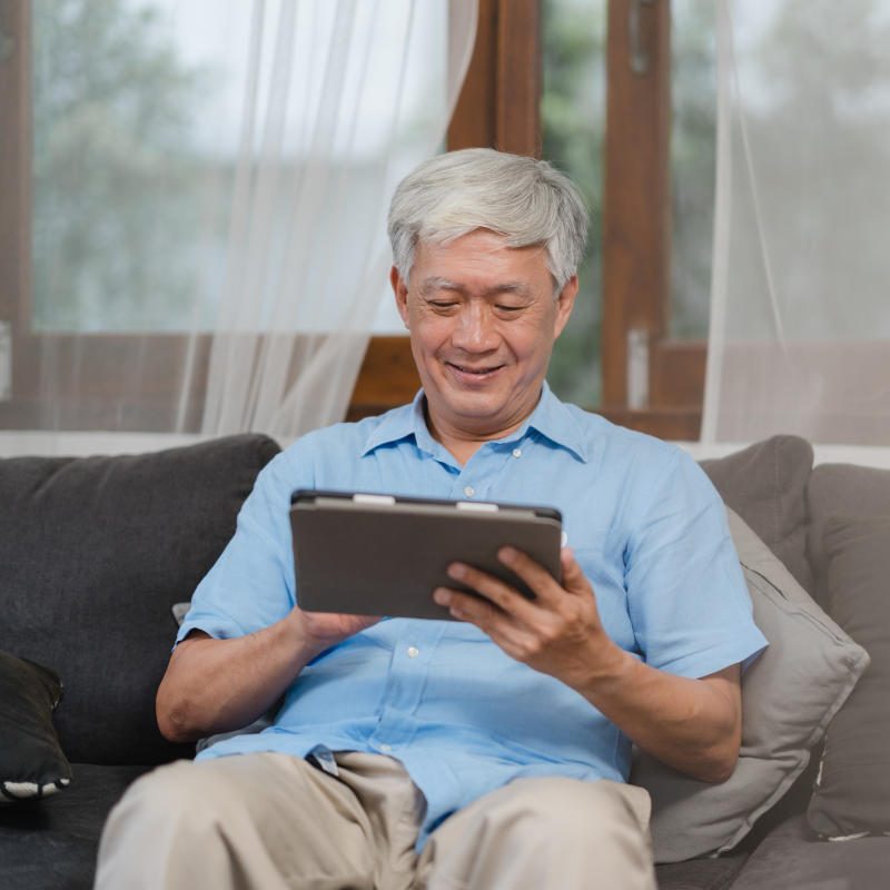 Asian senior men using tablet at home. Asian Senior Chinese male search information about how to good health on internet while lying on sofa in living room at home concept.